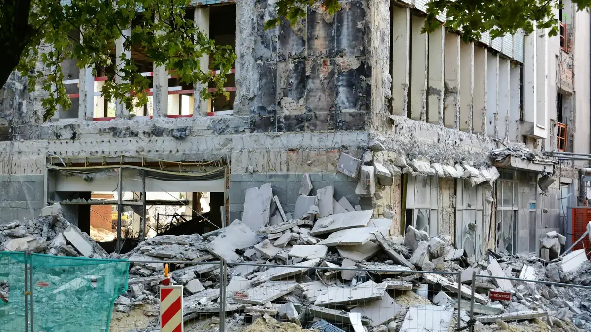 A concrete building part demolished behind safety fencing, one facade still standing