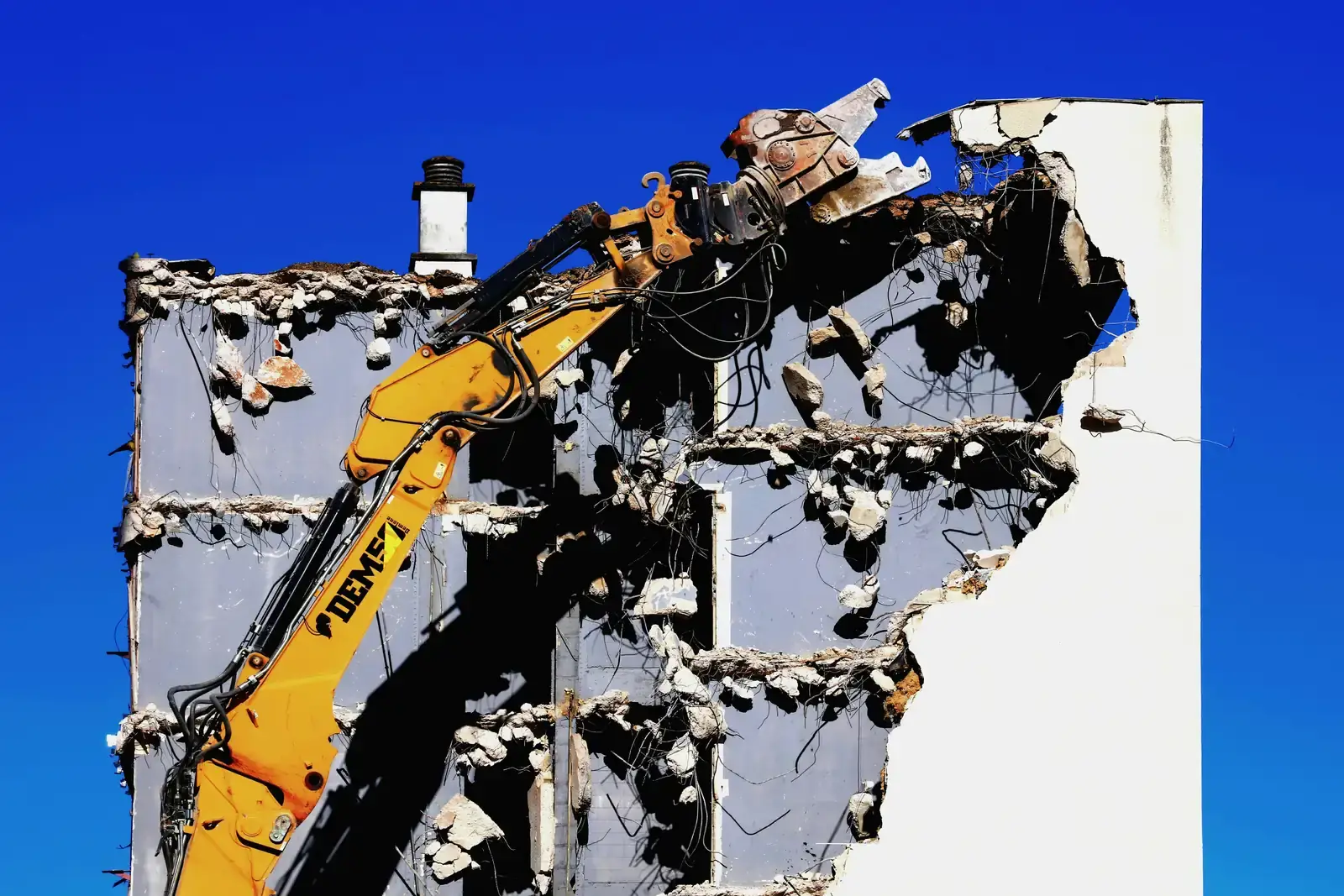 An excavator with hydraulic shears cutting into a concrete panel building