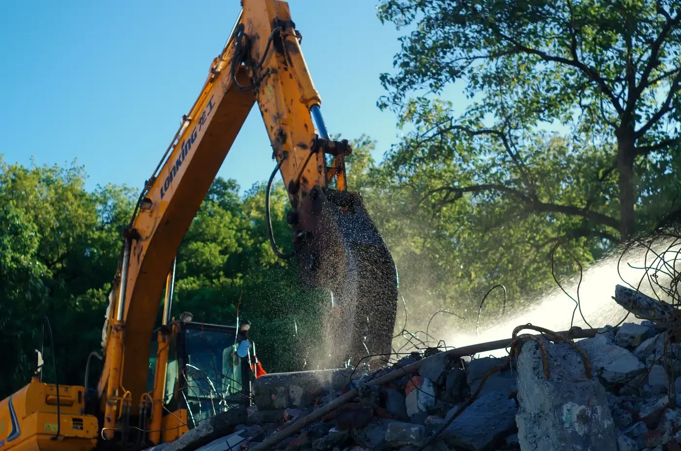 An excavator spraying water to suppress dust as it works into a brick wall