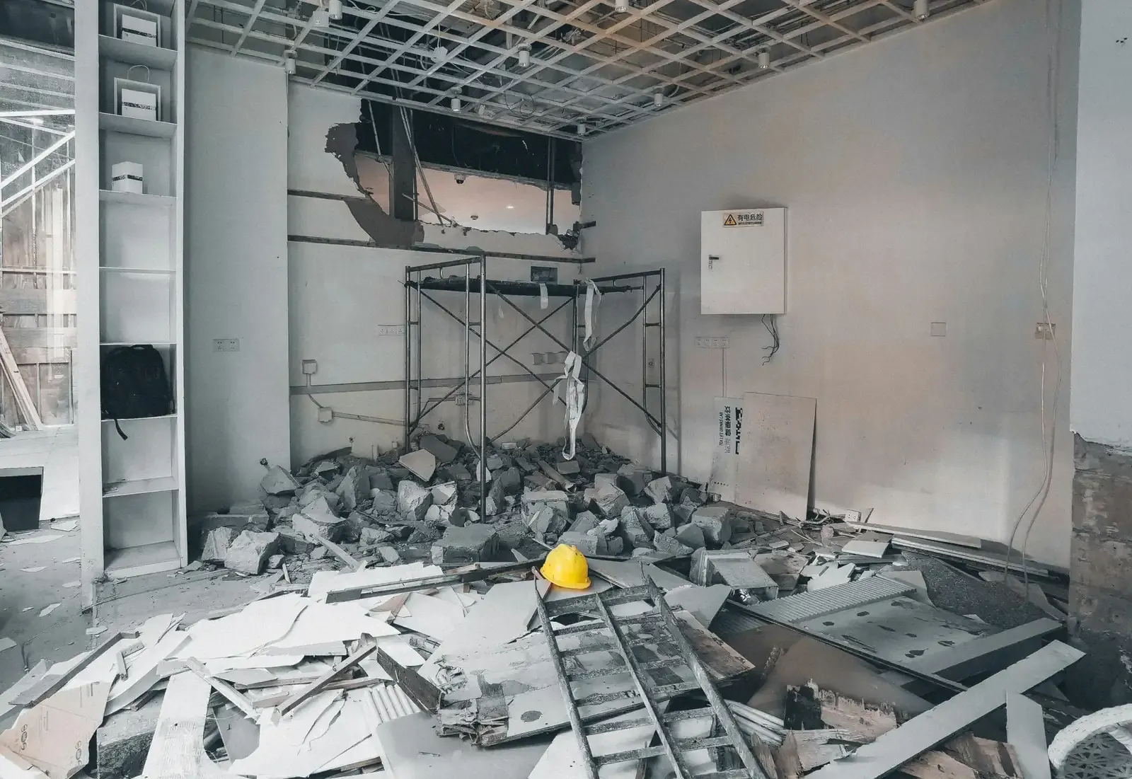 A room mid strip-out with the suspended ceiling grid partly down and a hard hat on the floor