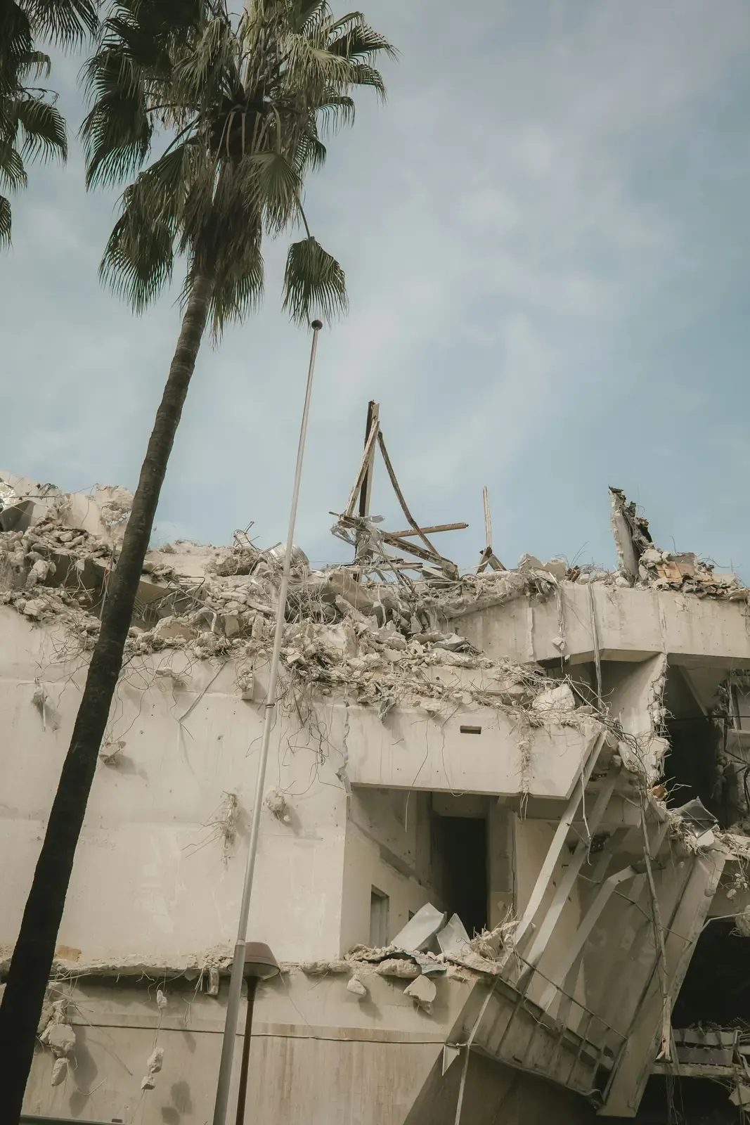 A partly demolished concrete building with palm trees standing in front of it