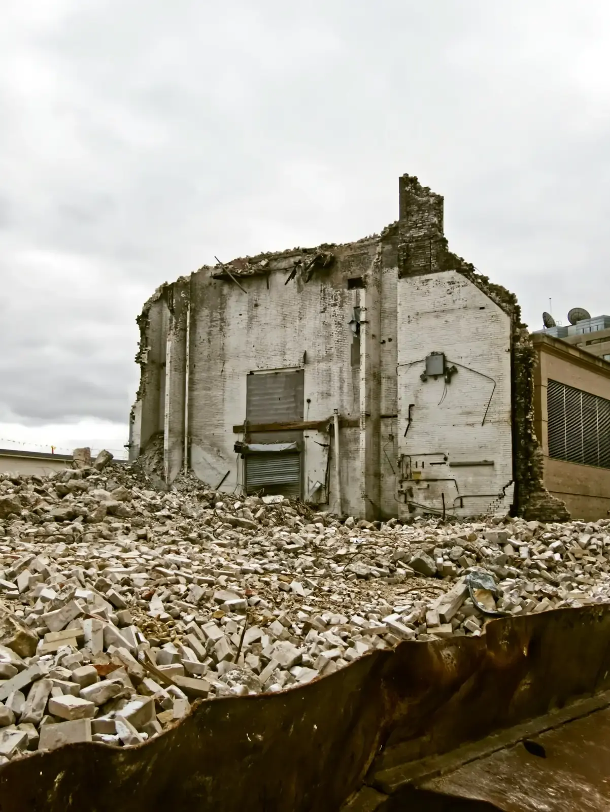 A white brick building part demolished, a field of rubble spread out in front of it